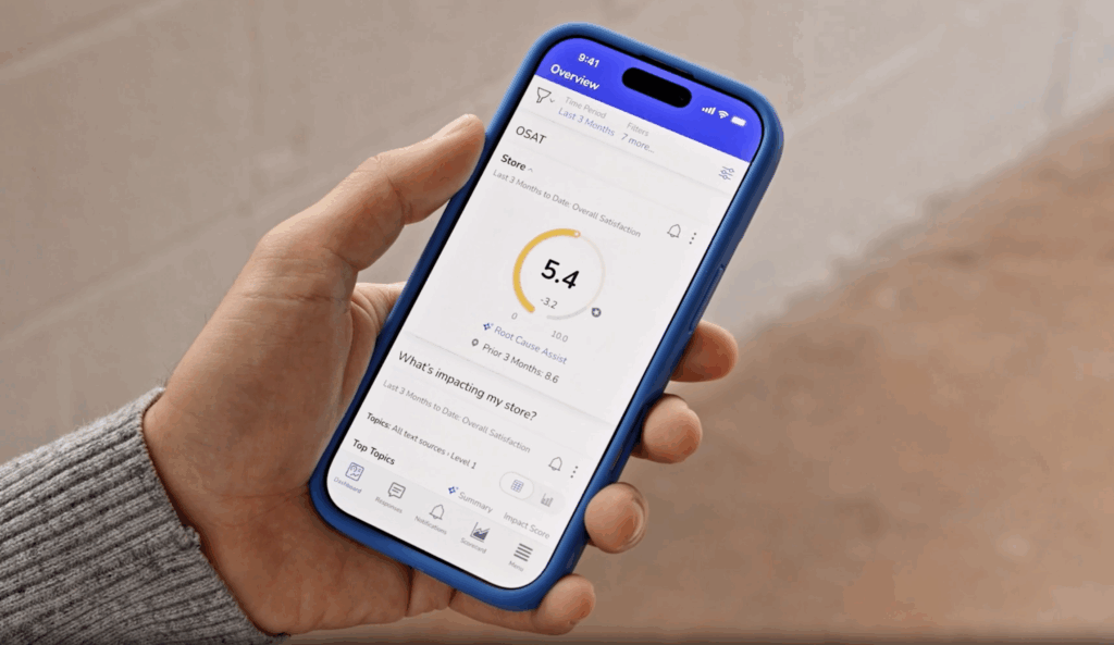 A person holding a smartphone with a blue case, displaying a health tracking app showing a score of 5.4 and various health metrics on the screen. The background is a blurred outdoor setting.